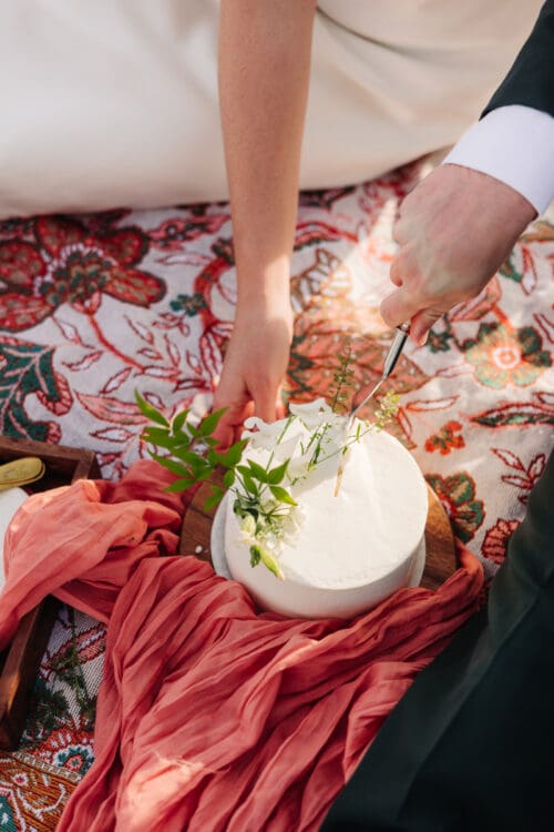 Hands arranging flowers and champagne on a picnic blanket during a mountain wedding celebration.