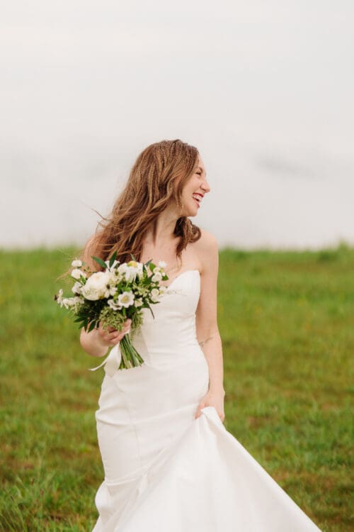 Bride smiling during a remote elopement in the Blue Ridge Mountains while holding a bouquet in an open field.