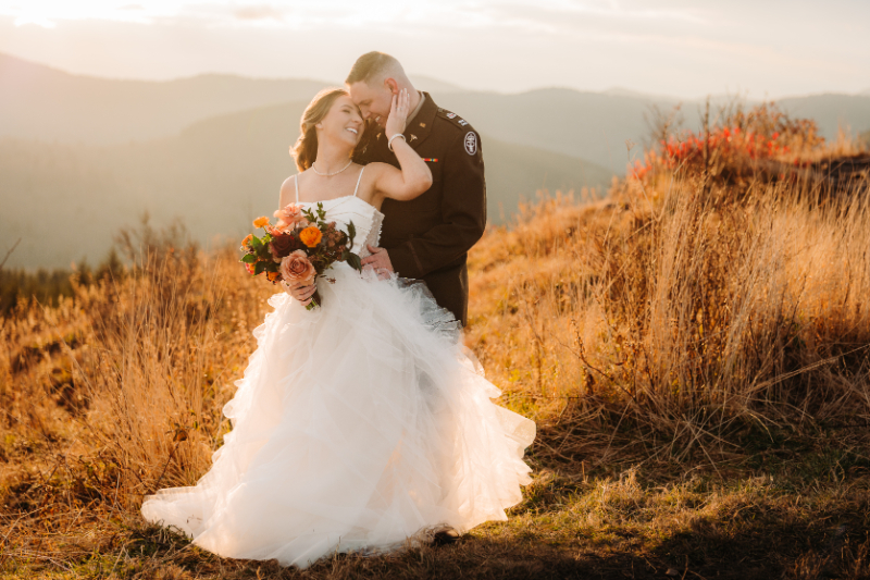 Couple embracing on a grassy mountain hillside with warm golden light and autumn tones