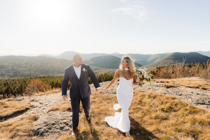Couple walking hand in hand on mountain overlook with sweeping Blue Ridge views and soft sunlight