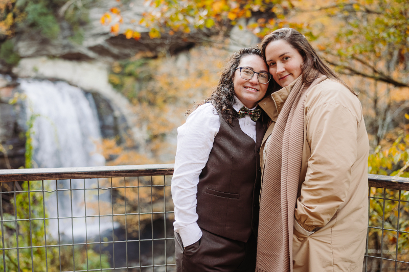 Couple standing near a waterfall during autumn, surrounded by Blue Ridge Mountains fall colors.
