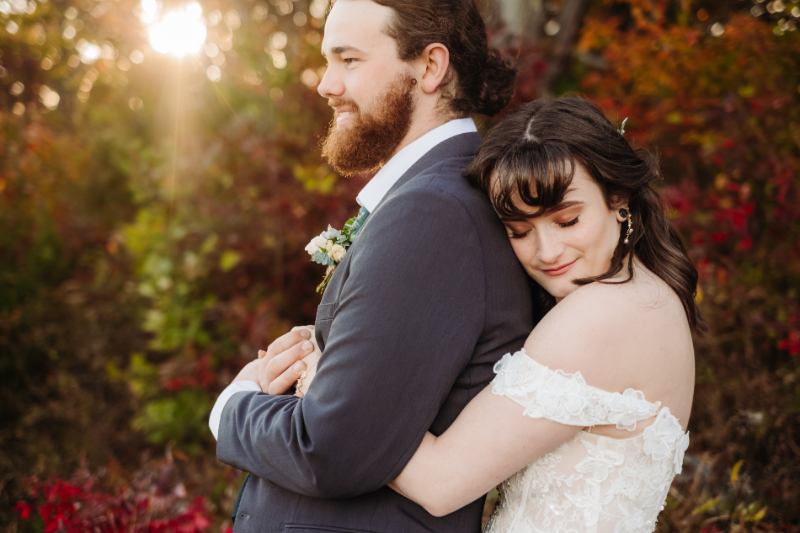 Bride hugging groom from behind during an intimate outdoor elopement surrounded by autumn foliage.