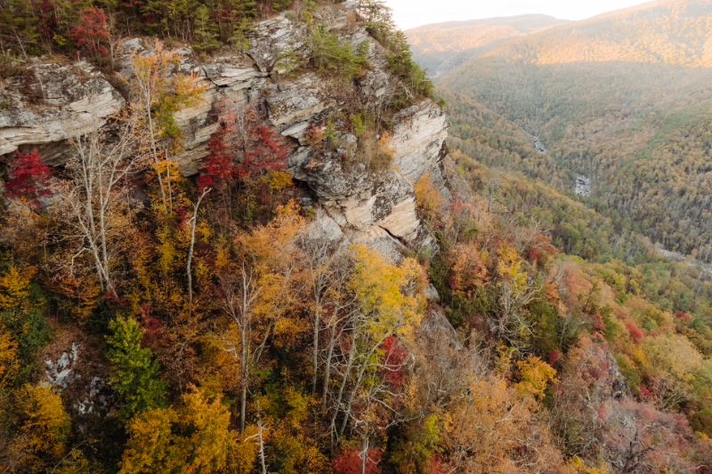 Aerial view of a rocky cliff overlooking mountains covered in autumn trees and rolling valleys.