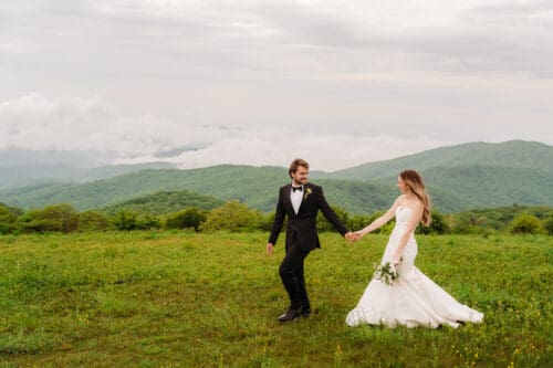 Couple walking hand in hand across Max Patch during their Hot Springs NC elopement with panoramic Blue Ridge Mountain views.