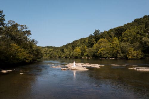 Aerial view of a bride standing on rocks in the French Broad River near Hot Springs NC, a beautiful location for adventurous elopement portraits.