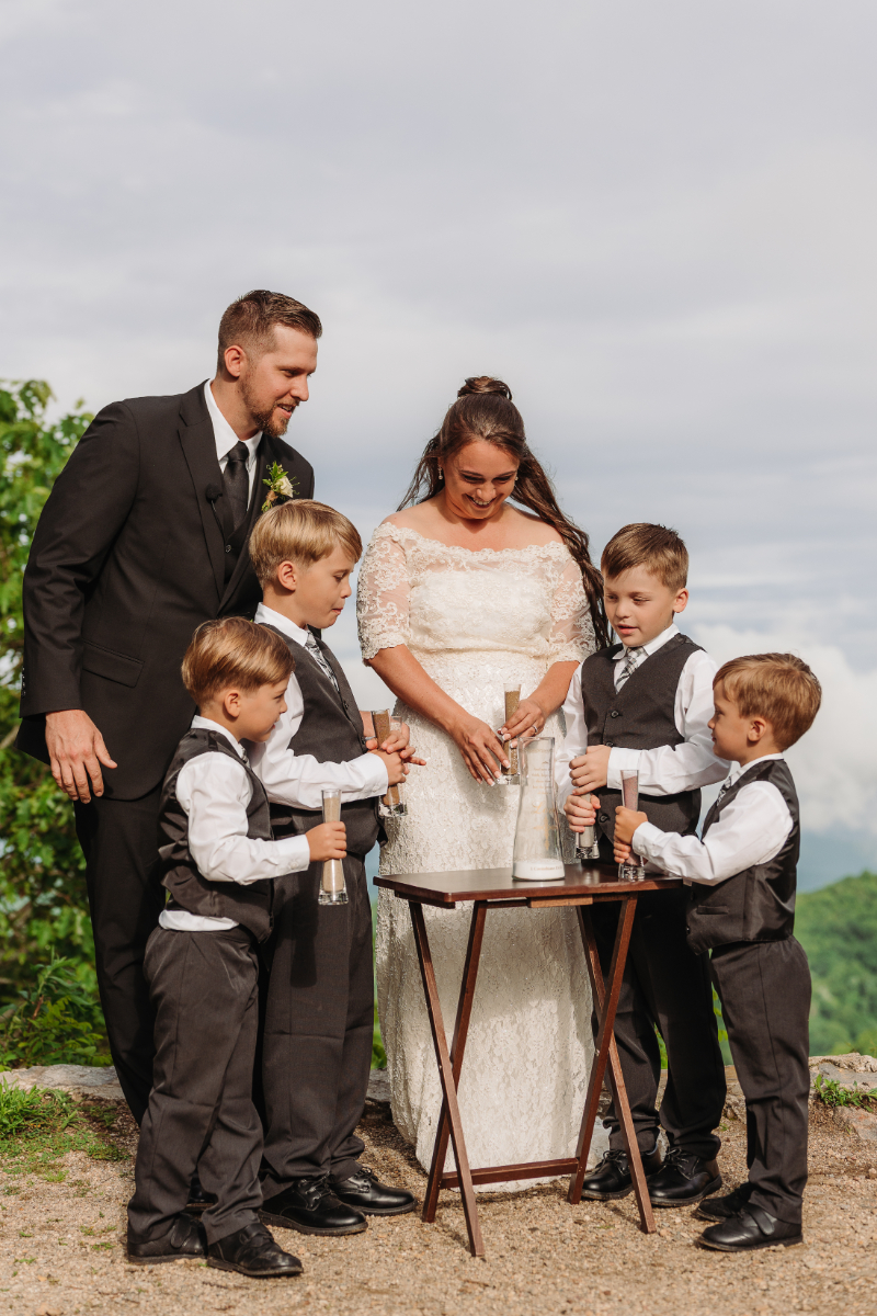 Couple and four children gather around a table during a unity sand ceremony at a mountain wedding.
