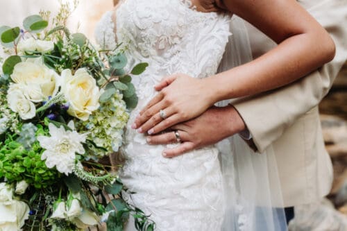 Close-up of the bride's bouquet and wedding rings as the couple embraces after exchanging vows.