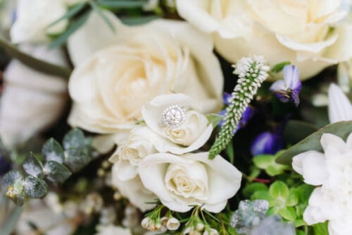 Close-up of a bridal bouquet with white roses and an engagement ring nestled among the flowers.