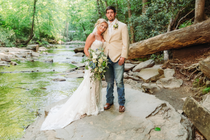 Newlyweds posing together on a rock beside a peaceful mountain creek after their ceremony.