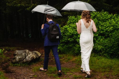 Bride and groom walking toward their ceremony with umbrellas on a rainy wedding day in the Blue Ridge Mountains.