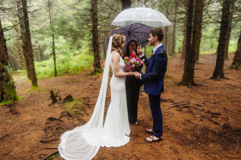 Bride and groom exchanging vows beneath umbrellas during a rainy wedding day forest elopement in Asheville.