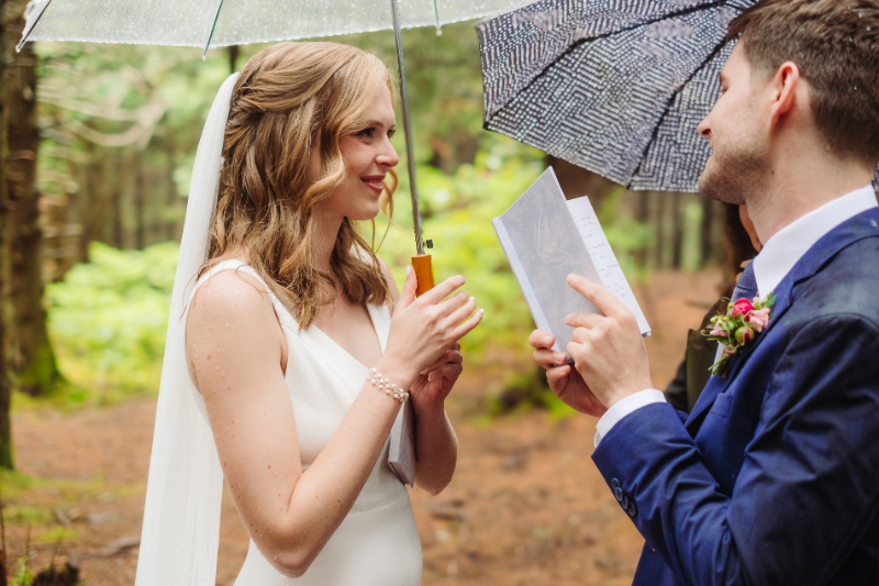 Bride and groom reading vows beneath umbrellas on a rainy wedding day during their Asheville elopement.