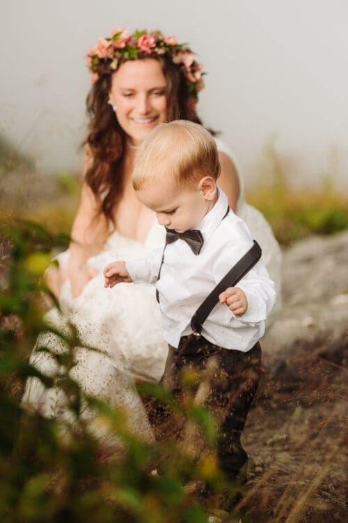 Young child explores wildflowers during a relaxed mountain wedding celebration.