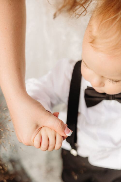 Close up of a parent holding their young child's hand during a wedding.