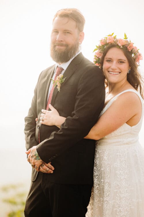 Bride hugs groom from behind while smiling during their mountain wedding portraits.