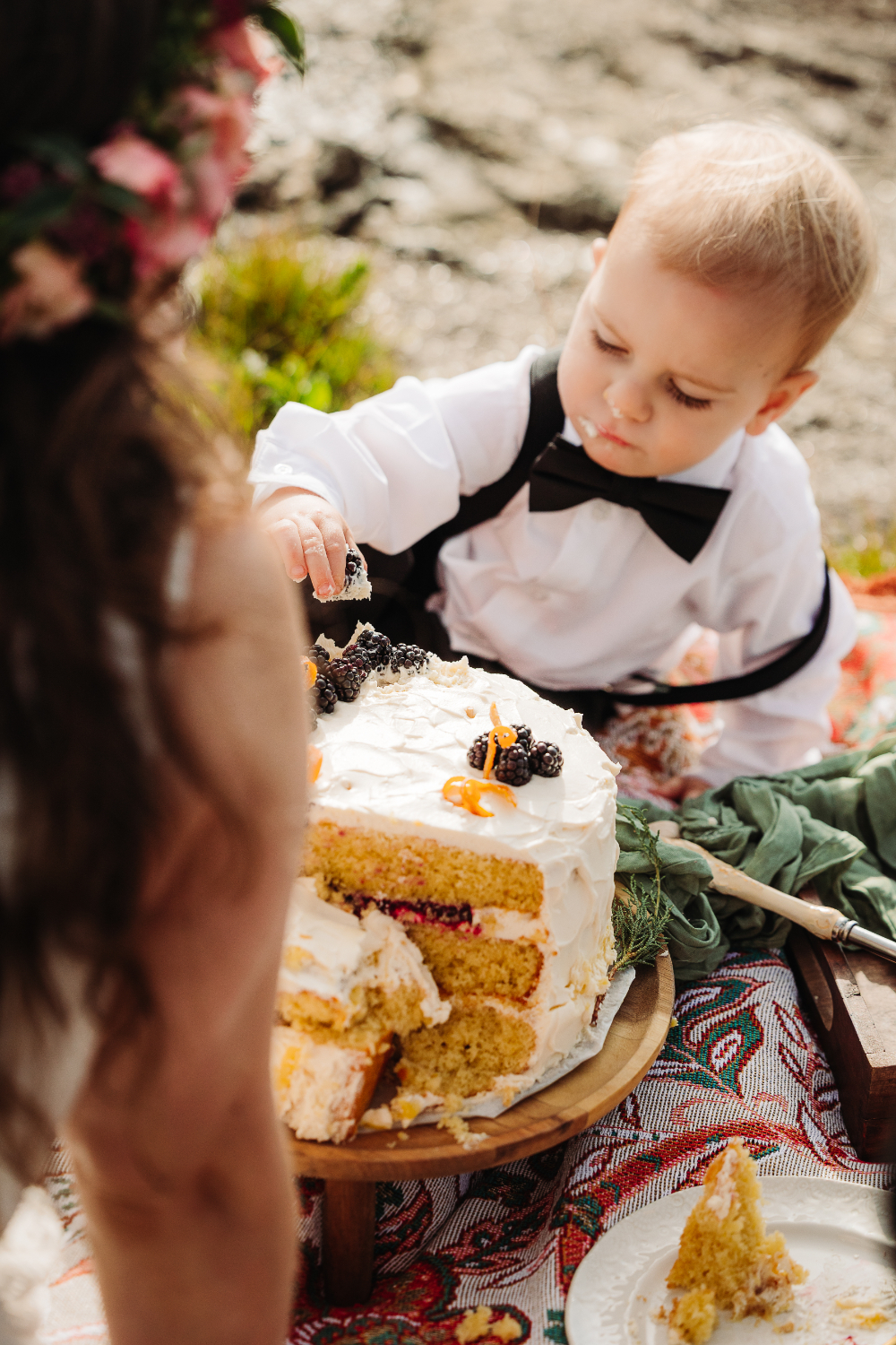 Young child reaches for wedding cake during a family focused mountain celebration.
