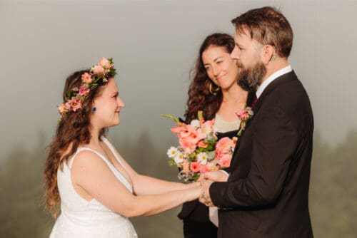 Bride and groom exchange bouquets during their outdoor wedding ceremony with their officiant.