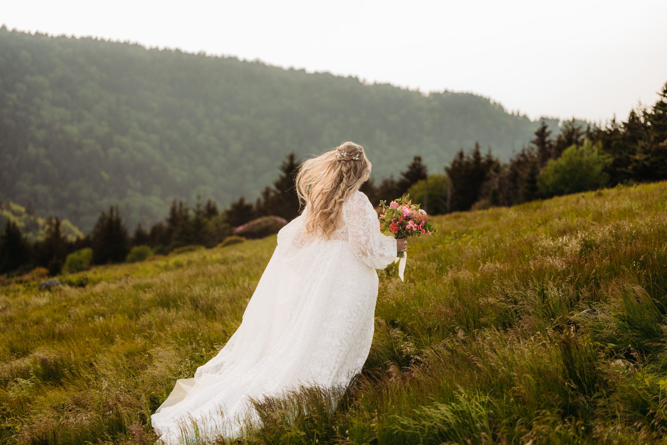 Bride walking through a windswept mountain meadow carrying a colorful wedding bouquet