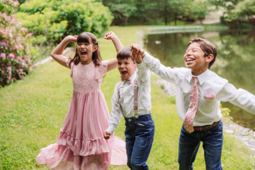 Children laughing and playing together beside a pond during a relaxed outdoor family elopement celebration.