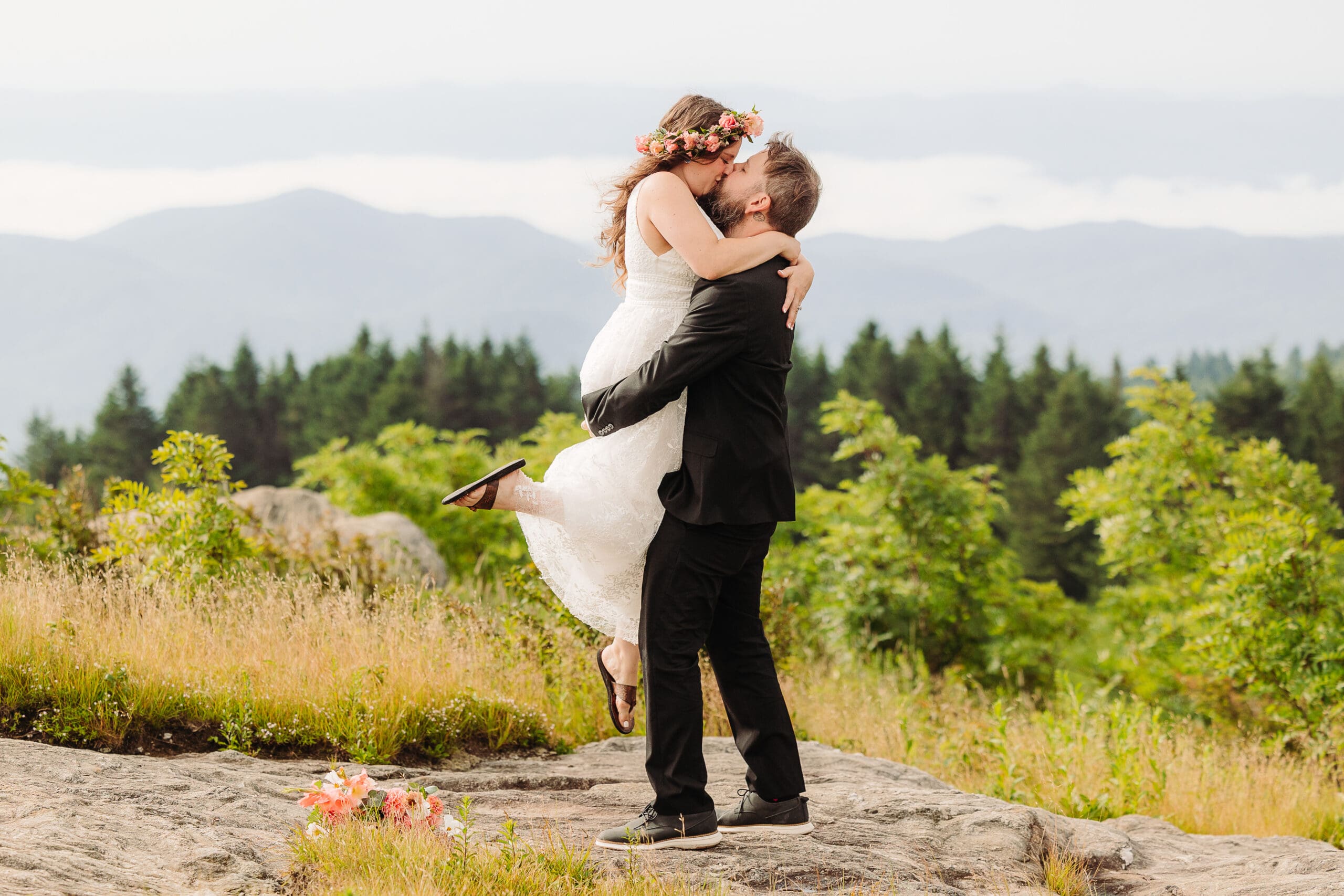 Groom lifting and kissing his bride with layered Blue Ridge Mountains in the background