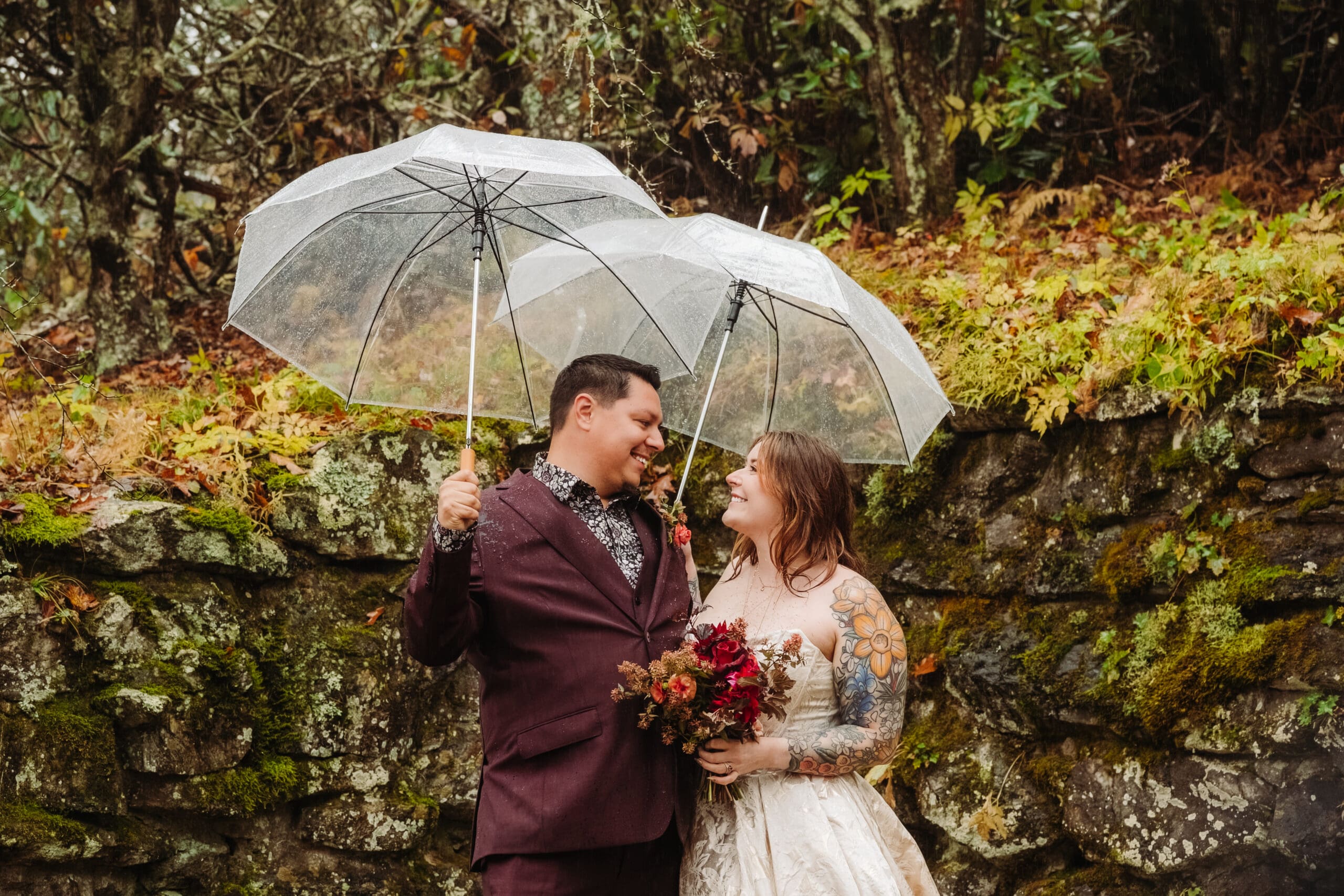 Couple laughing with their officiant beneath umbrellas during a rainy fall mountain elopement