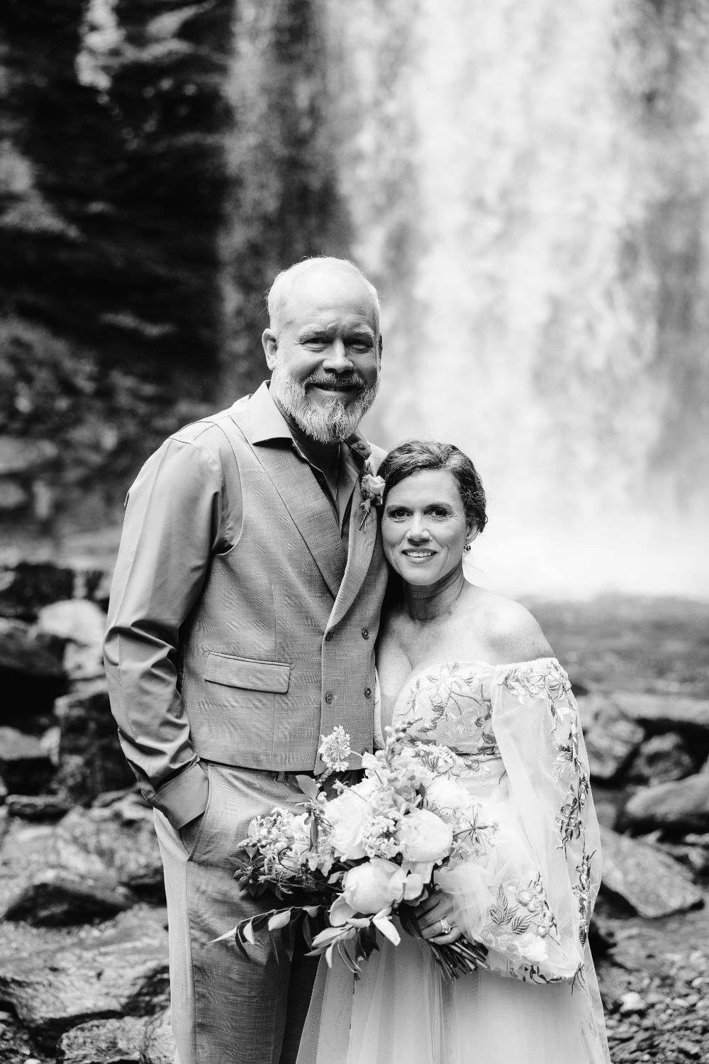 Newlywed couple smiling together in front of a waterfall after their intimate outdoor ceremony.