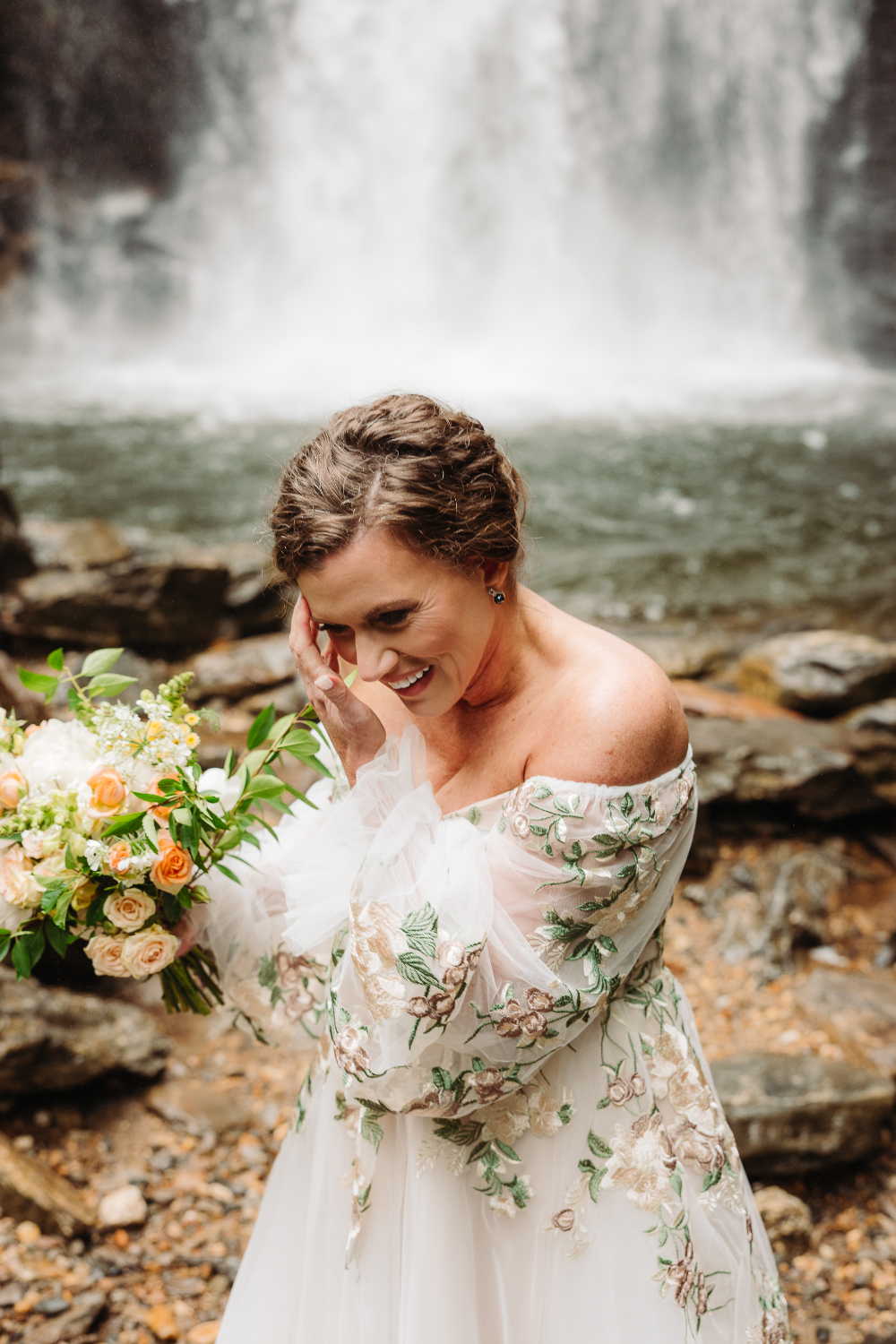 Bride holding her bouquet beside a mountain stream during her romantic wedding over 40.