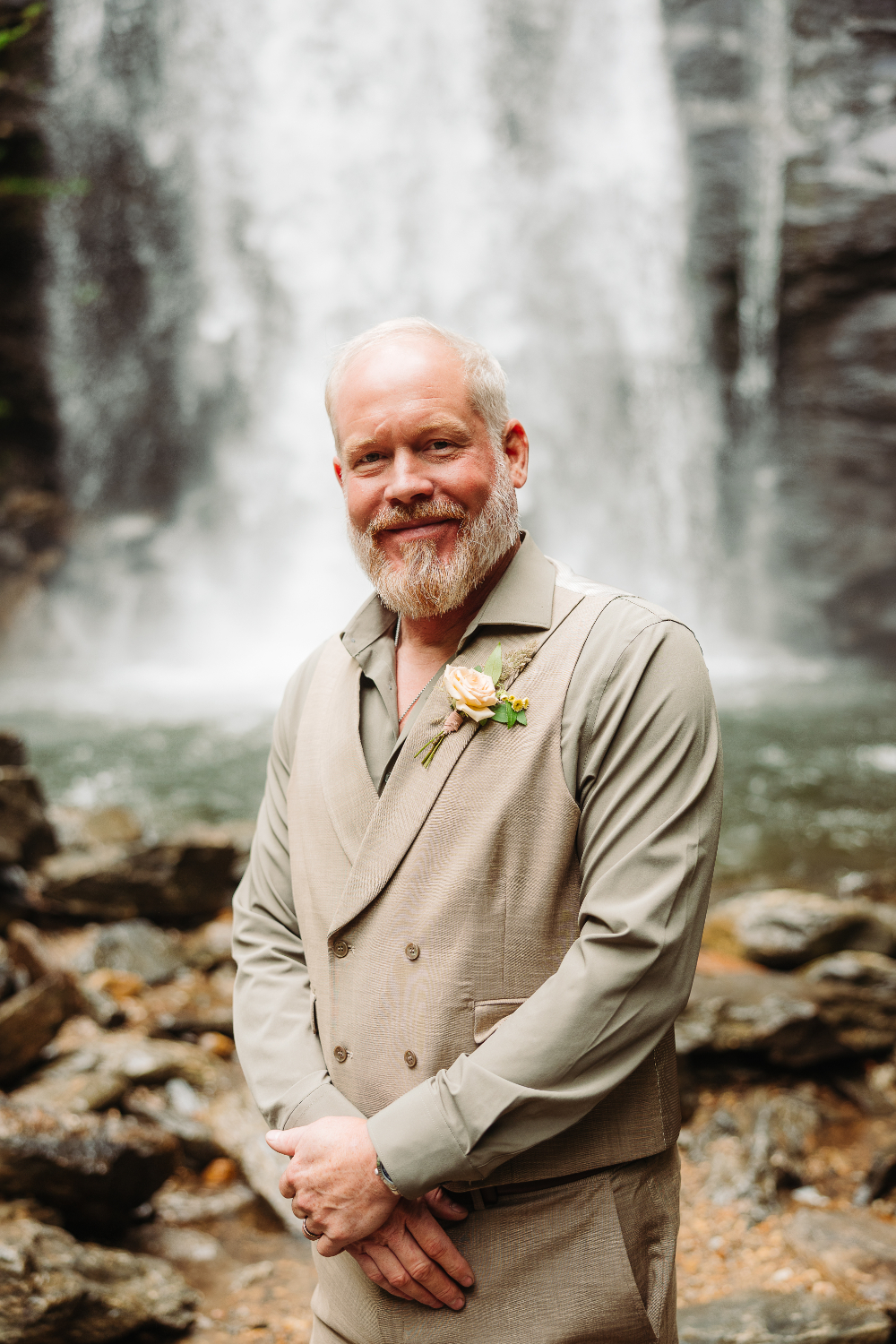 Smiling groom standing near a waterfall during an intimate wedding over 40 in the mountains.
