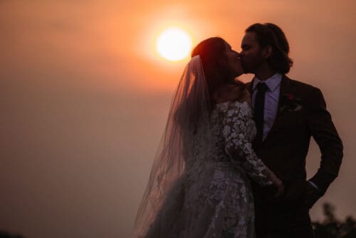 Couple sharing a sunset kiss during their Asheville elopement with the sun glowing behind the mountains.