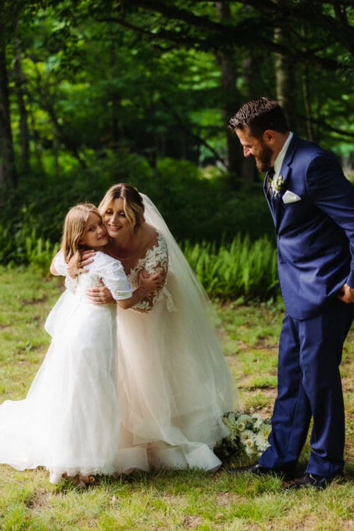 Bride sharing a sweet moment with a young girl while the groom smiles nearby.