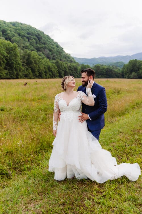 Bride and groom sharing a loving moment together in a grassy mountain meadow surrounded by forest.