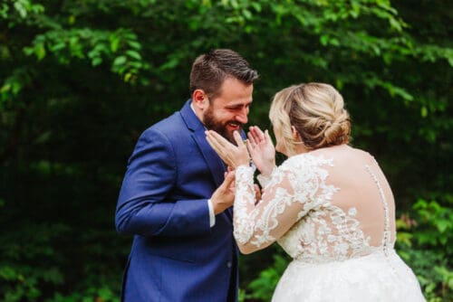 Groom smiling at his bride during an intimate wedding moment surrounded by lush greenery.