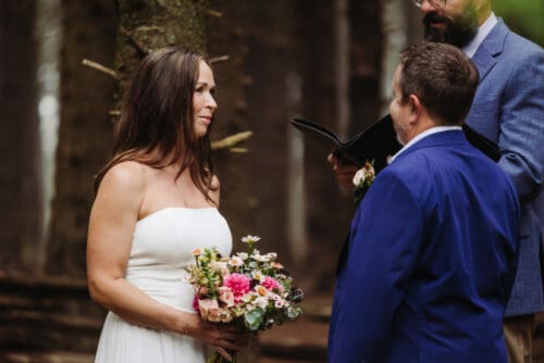 Bride holding her bouquet during a peaceful forest ceremony, surrounded by intimate wedding ideas and nature.