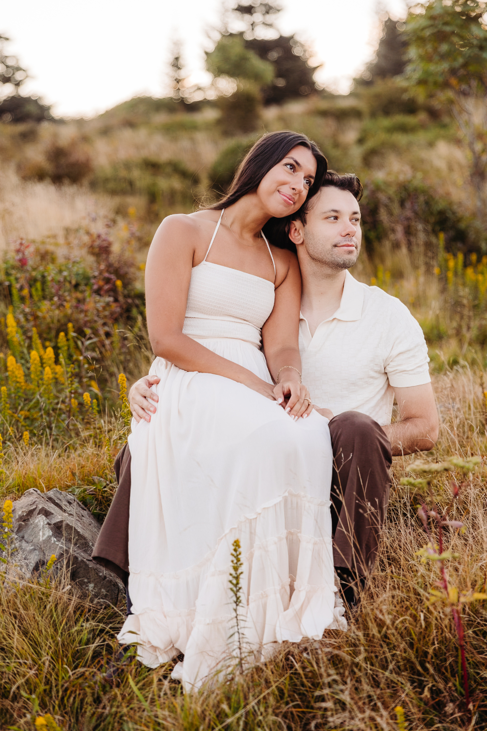 Couple cuddles in a mountain meadow filled with wildflowers during their romantic sunset engagement session.